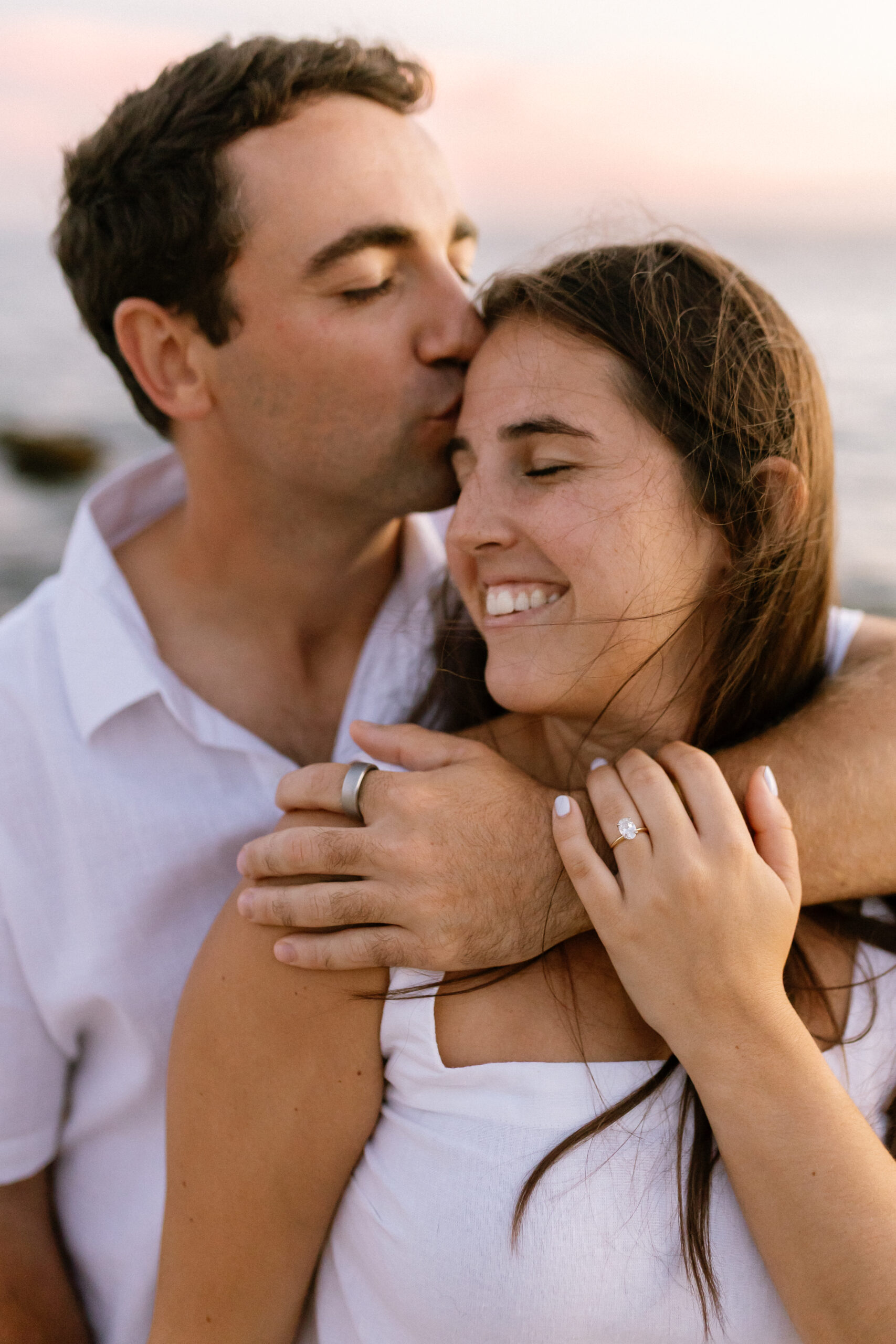 Taylor+Owen Engagement Gallery. Engaged couple embrace on breezy beach.
